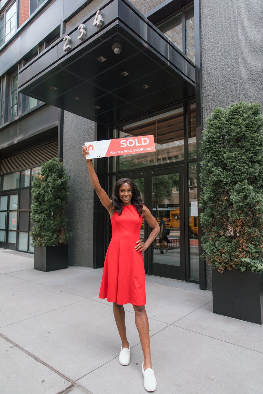 woman in red dress holding sold sign above her head